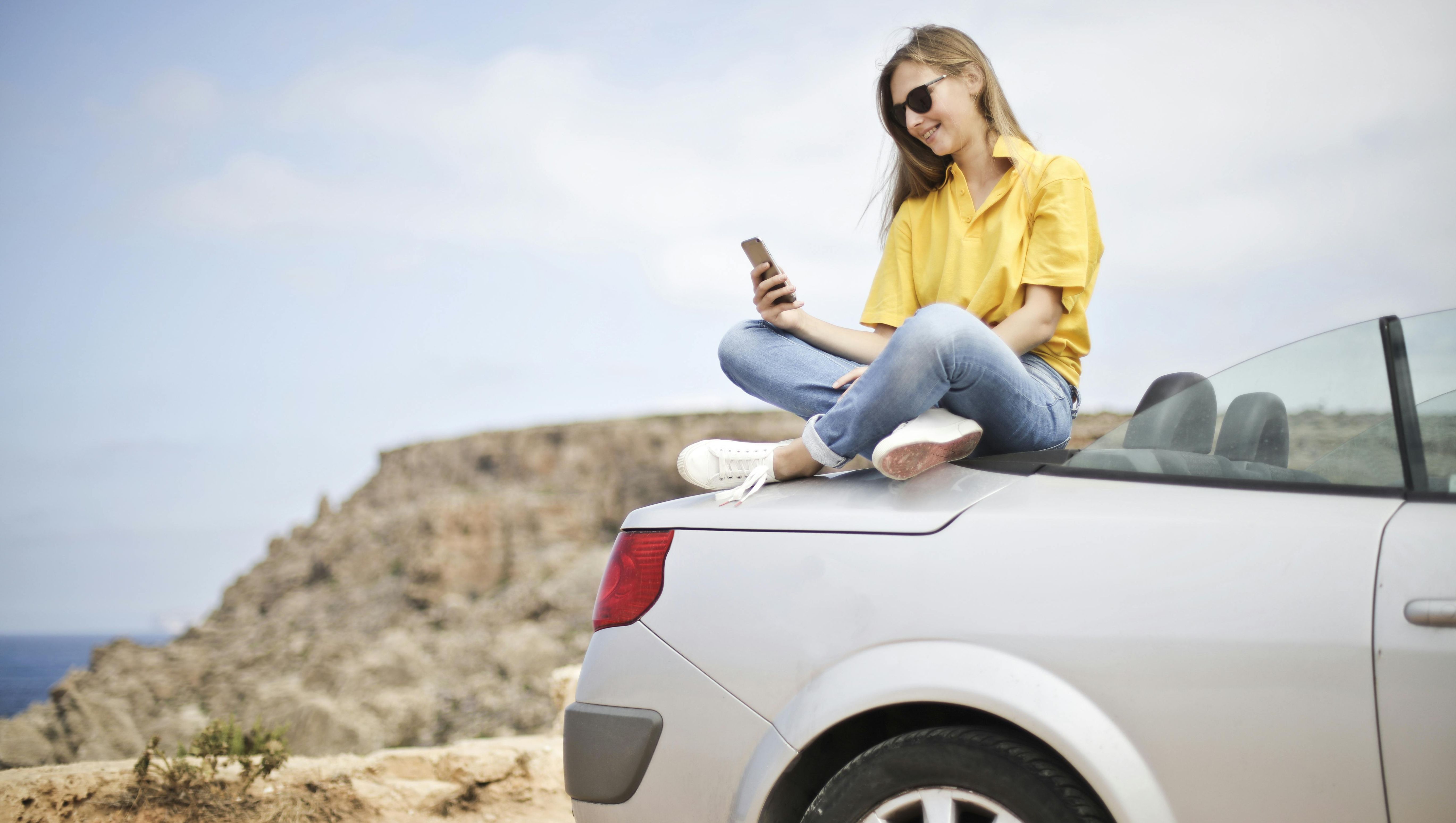 kvinna i gul tröja sitter på bilhuven